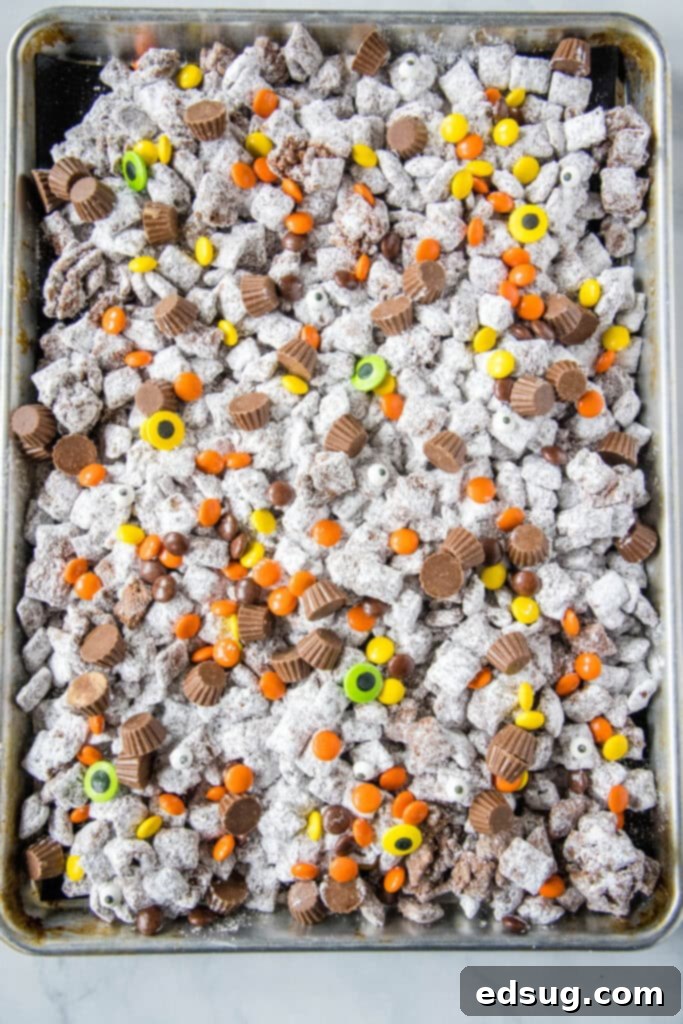 Spooky Halloween Muddy Buddies 6 looking down on a tray of halloween puppy chow with a hand reaching for a piece