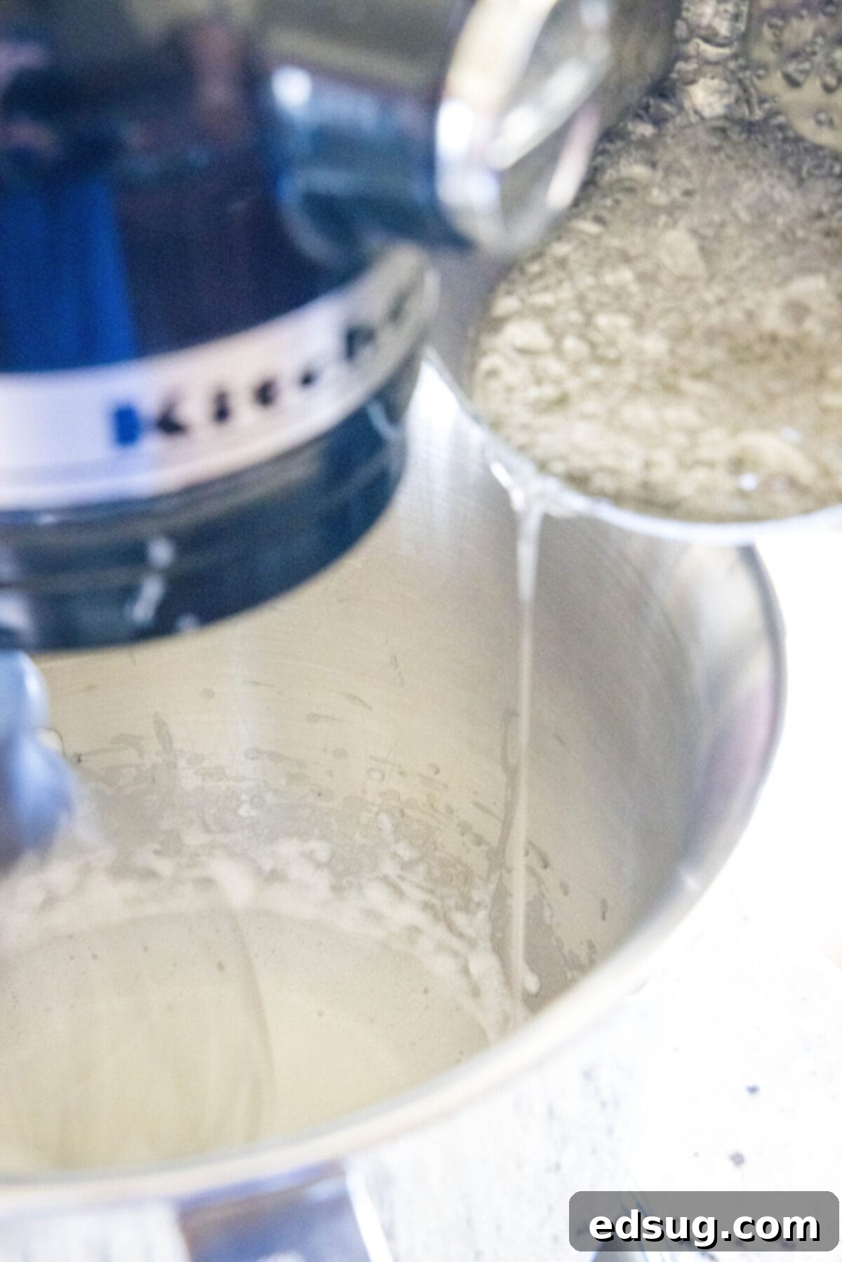 Boiling sugar being poured into beat egg whites in a stand mixer