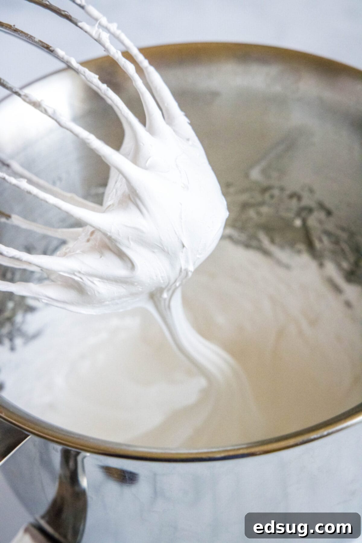 A stand mixer whisk attachment being pulled out of bowl filled with marshmallow fluff