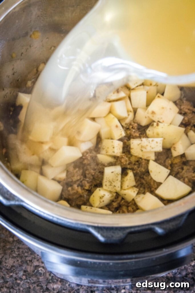 This copycat Olive Garden Zuppa Toscana is rich, hearty, healthy, loaded with potatoes and sausage, and easy to make in the Instant Pot. Chicken broth being poured into a pot full of sausage and potatoes
