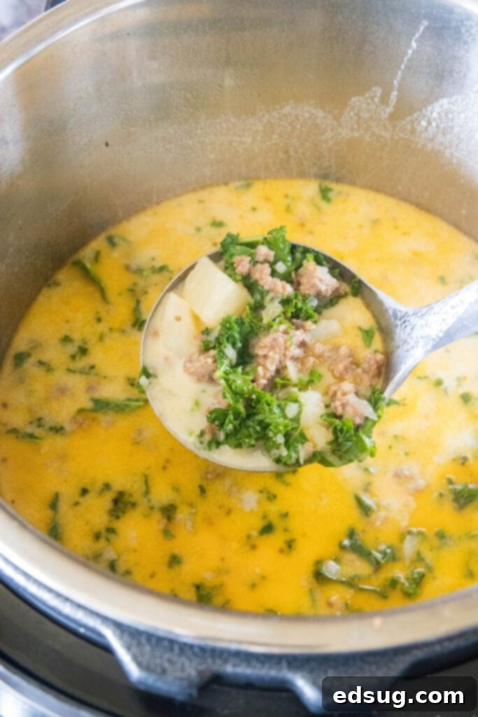This copycat Olive Garden Zuppa Toscana is rich, hearty, healthy, loaded with potatoes and sausage, and easy to make in the Instant Pot. A ladle full of Zuppa Toscana with a pot full of it in the background