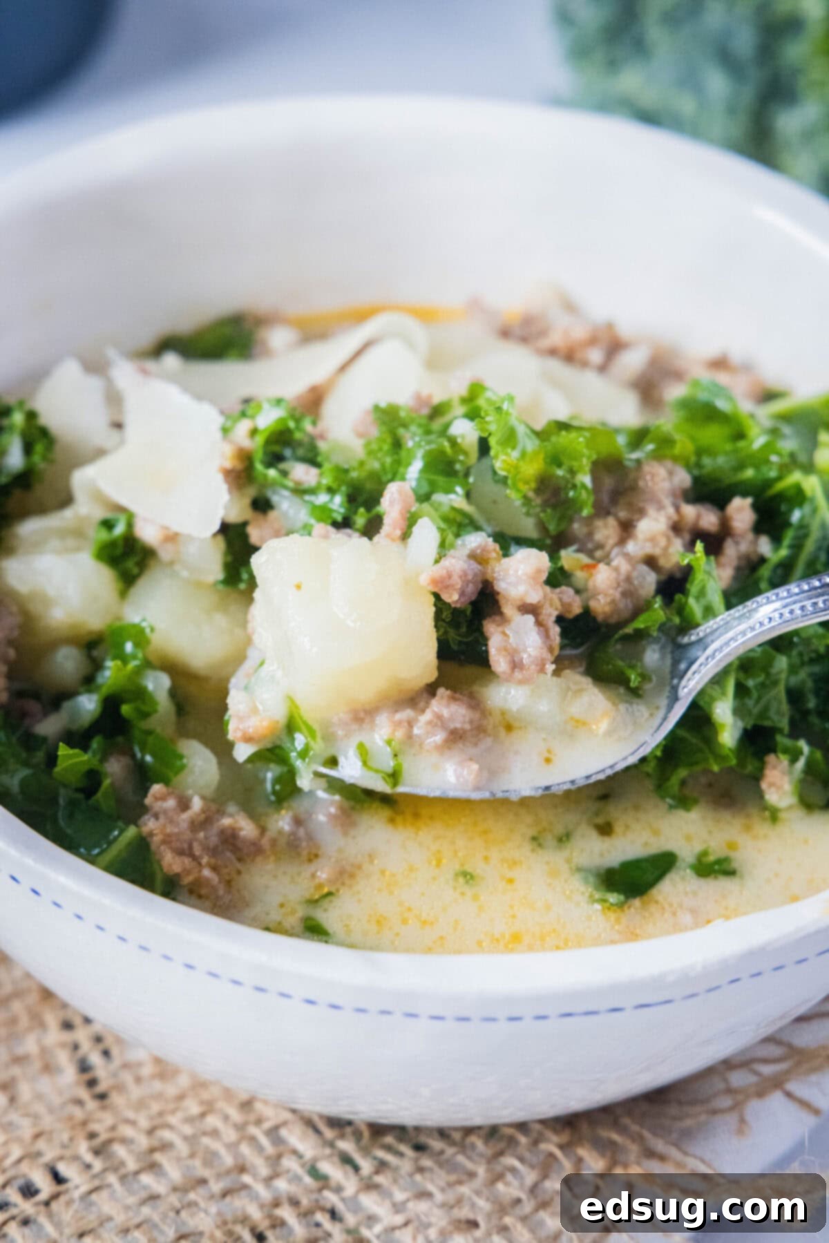 This copycat Olive Garden Zuppa Toscana is rich, hearty, healthy, loaded with potatoes and sausage, and easy to make in the Instant Pot. A bowl of Zuppa Toscana with a spoon taking a spoonful out