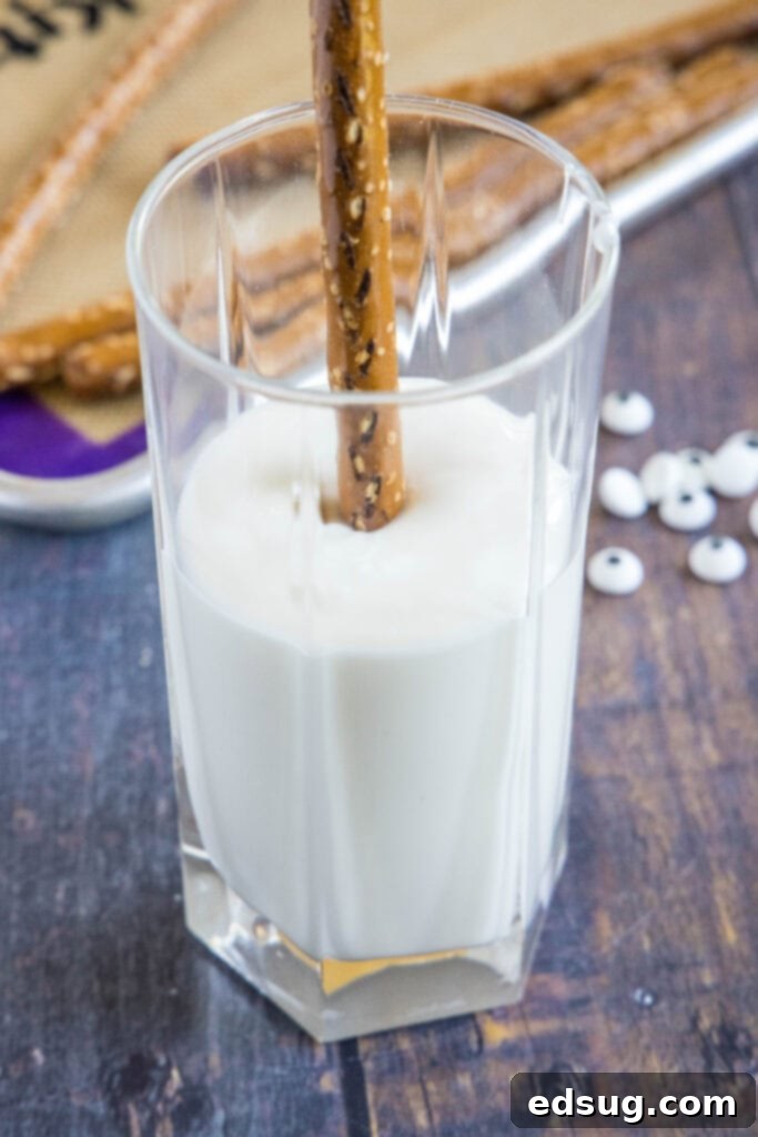 Bandaged Bites 4 A hand gently dipping a pretzel rod into a tall glass filled with perfectly melted white chocolate.
