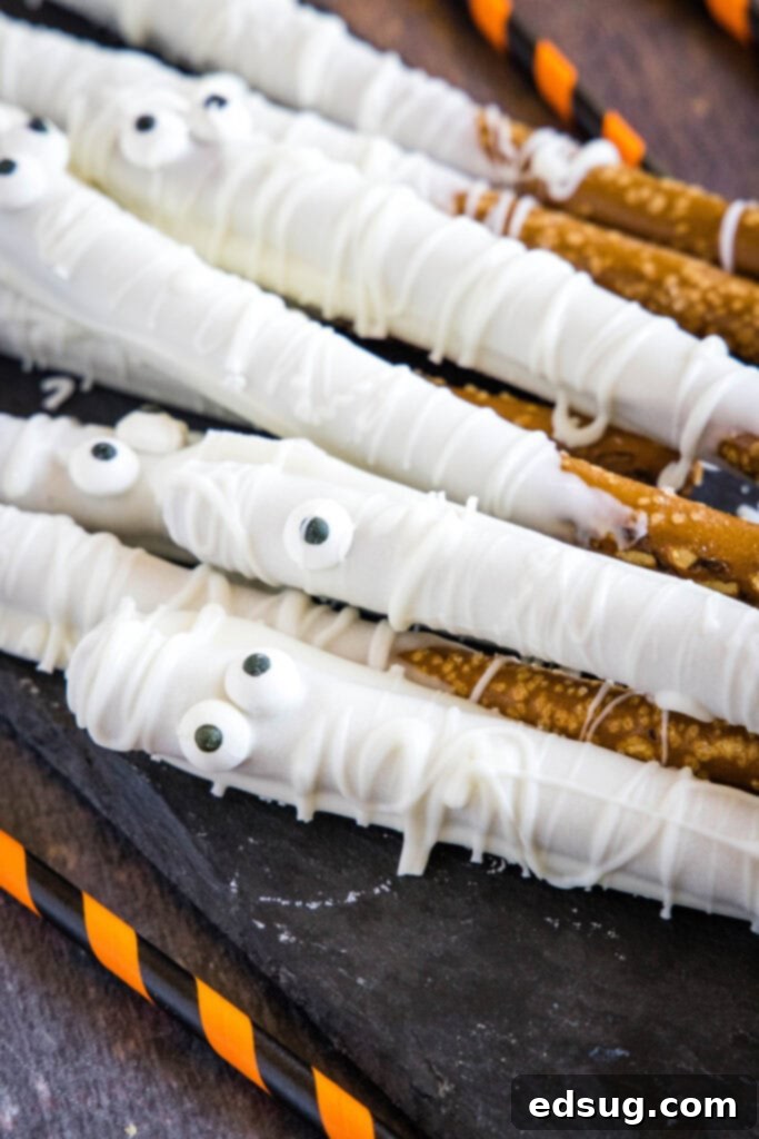 Bandaged Bites 6 A festive display of finished white chocolate mummy pretzel rods arranged artfully on a serving tray, perfect for a Halloween party.