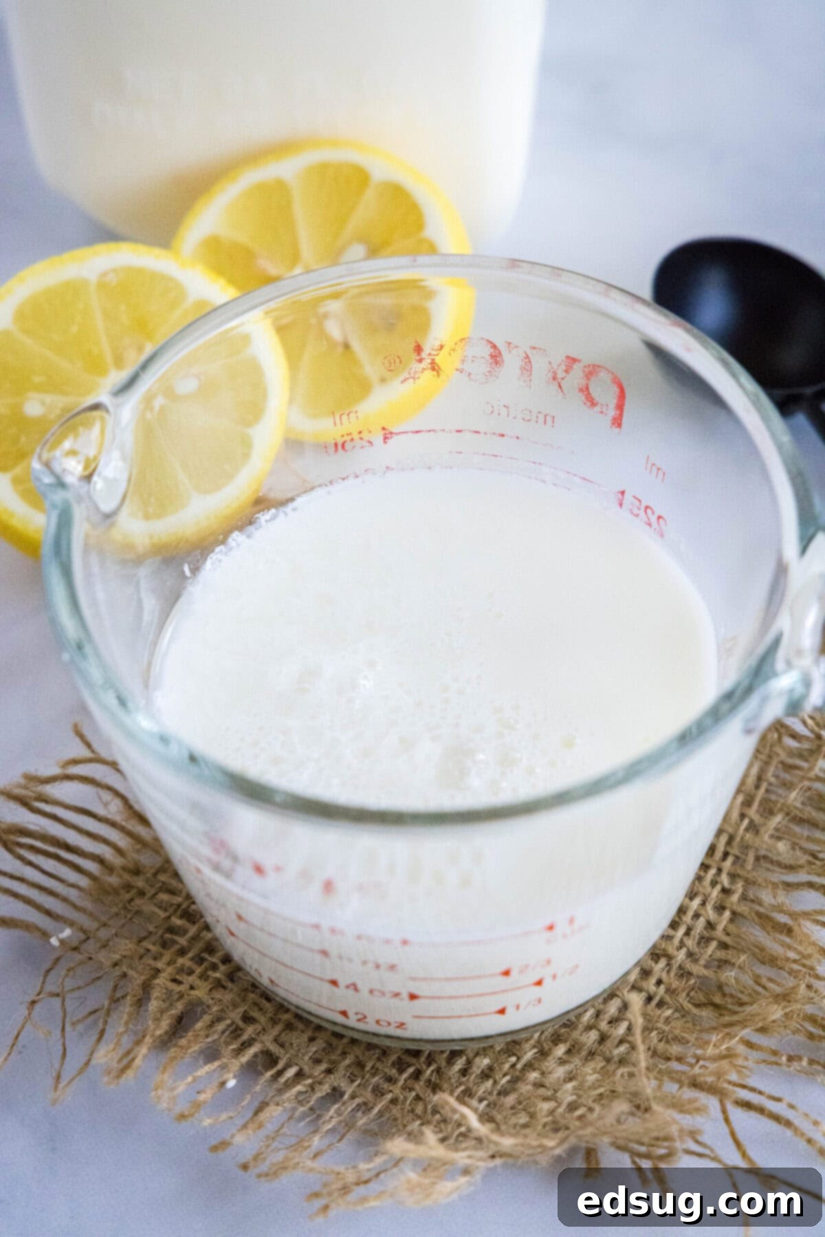 This 2-ingredient homemade buttermilk recipe is super creamy, perfectly tangy, and can be used in any recipe that calls for buttermilk.  A pyrex of homemade buttermilk with lemon slices in the background, ready to be used in baking or cooking.