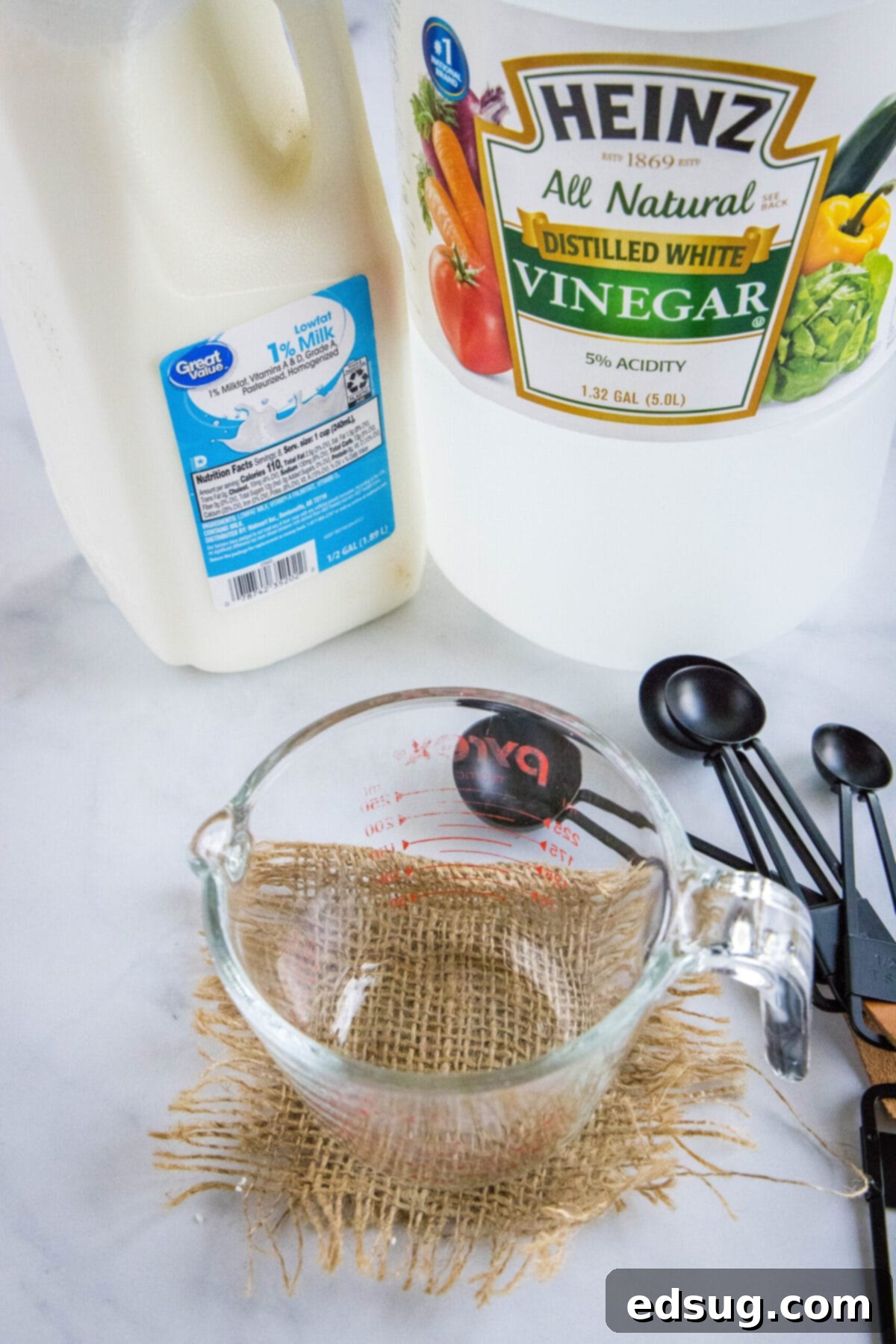This 2-ingredient homemade buttermilk recipe is super creamy, perfectly tangy, and can be used in any recipe that calls for buttermilk.  Overhead view of the essential ingredients for homemade buttermilk: a bottle of distilled white vinegar, a carton of milk, a clear measuring cup, and measuring spoons.