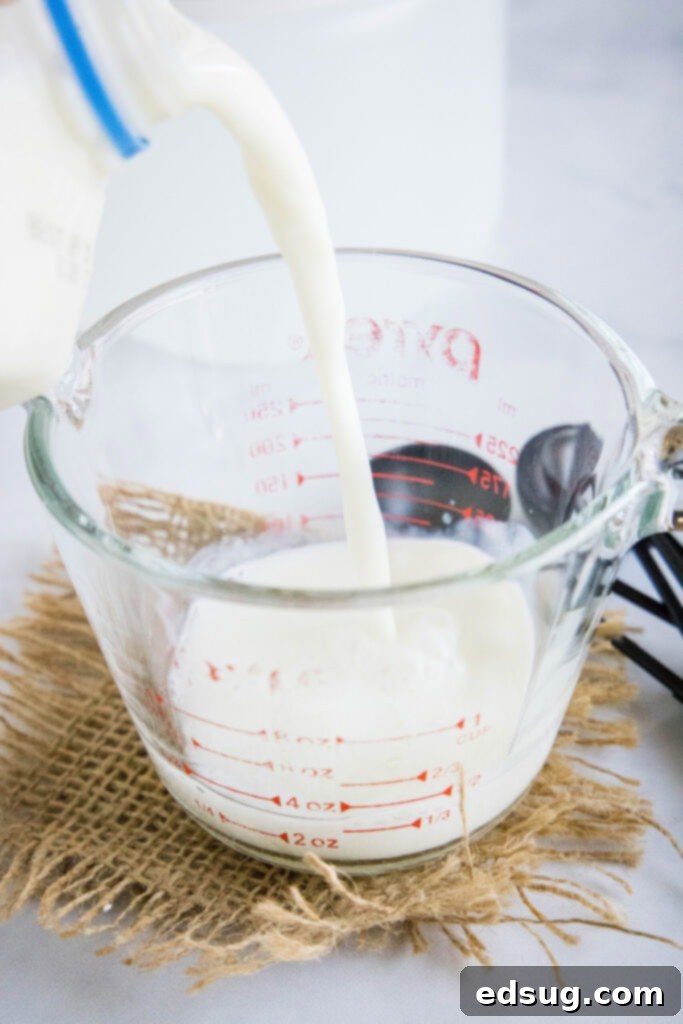 This 2-ingredient homemade buttermilk recipe is super creamy, perfectly tangy, and can be used in any recipe that calls for buttermilk.  Milk being poured into a pyrex measuring cup already containing an acidic ingredient for homemade buttermilk.