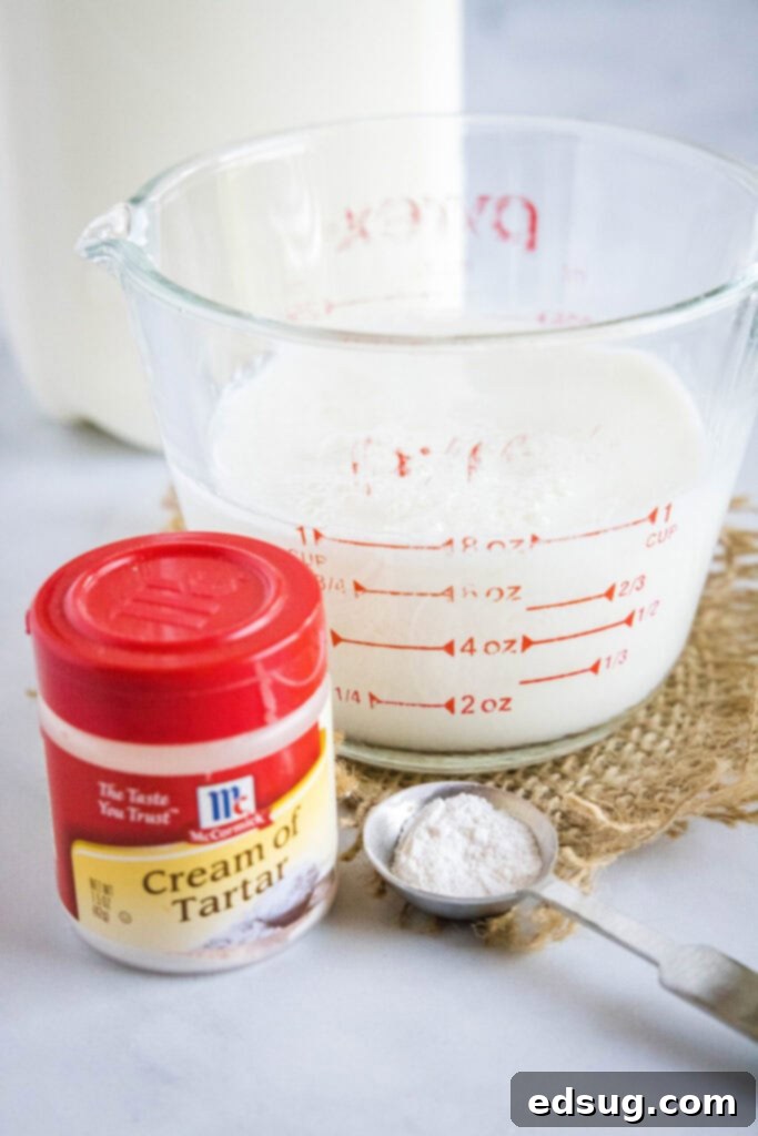 This 2-ingredient homemade buttermilk recipe is super creamy, perfectly tangy, and can be used in any recipe that calls for buttermilk.  A pyrex filled with milk and acid, a carton of milk, a container of cream of tartar, and a measuring spoon with cream of tartar in it, illustrating the ingredients for homemade buttermilk.