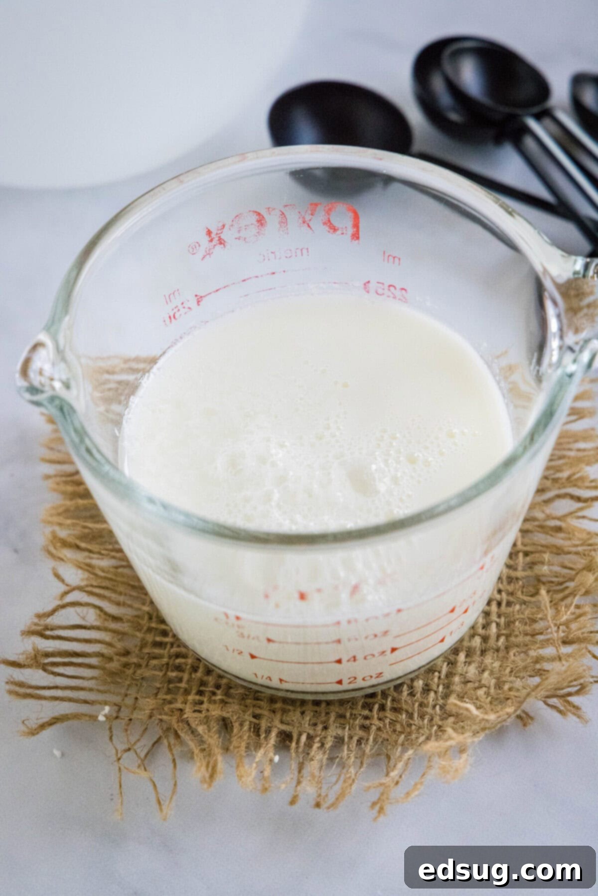 This 2-ingredient homemade buttermilk recipe is super creamy, perfectly tangy, and can be used in any recipe that calls for buttermilk.  A pyrex of homemade buttermilk with measuring spoons in the background, ready for use.