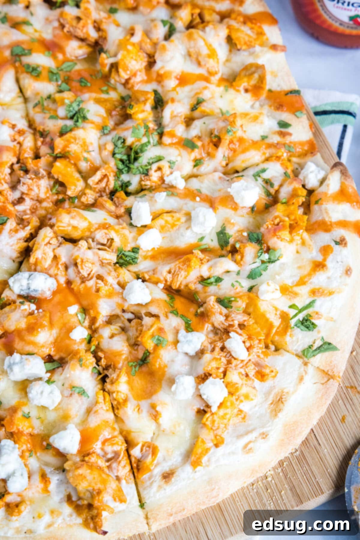 Overhead view of a delicious buffalo chicken pizza topped with blue cheese crumbles and fresh parsley, already cut into perfect slices, showcasing the melted cheese and vibrant chicken.