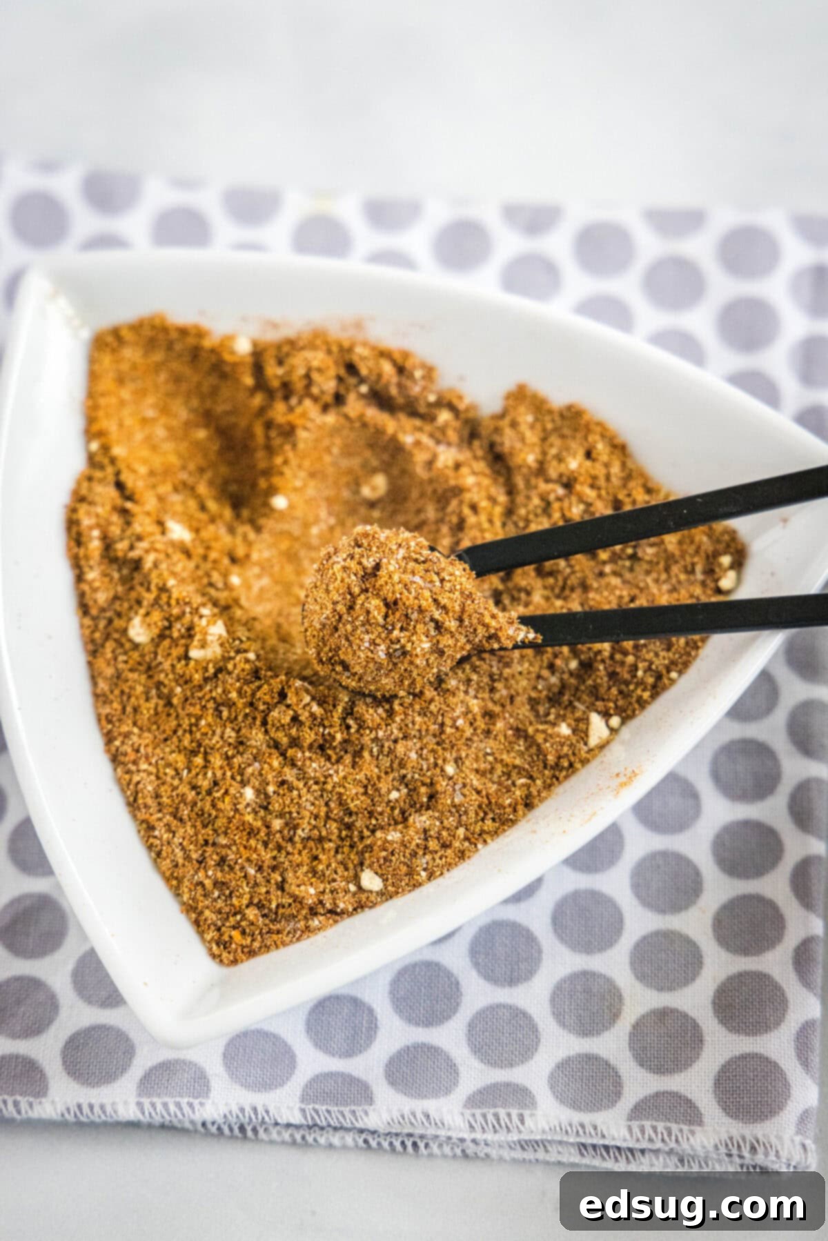Overhead view of a triangular bowl of fajita seasoning with a serving spoon