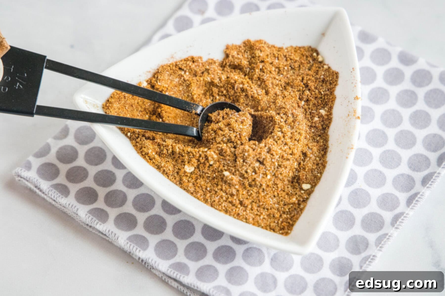 A triangular bowl of fajita seasoning with a spoon in it