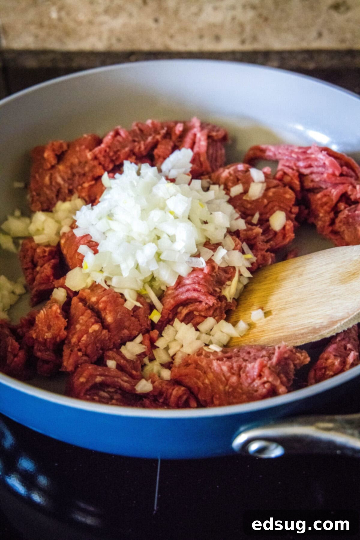 The initial step of homemade sloppy joes: raw beef and onions being mixed and cooked in a skillet. Raw lean ground beef and chopped yellow onions being mixed and cooked together in a hot skillet, as they begin to brown.