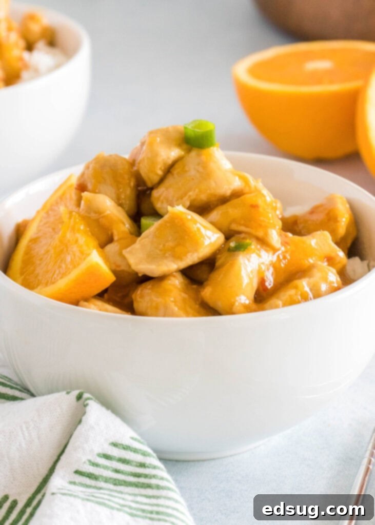 Zesty Orange Chicken 6 A close-up of a white bowl filled with glistening orange chicken, garnished with green onions.