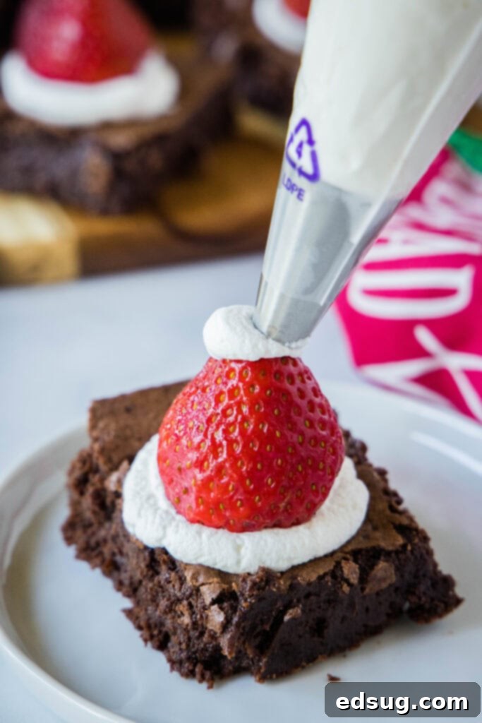 Piping a white frosting tip onto the top of a strawberry to complete the Santa hat look.