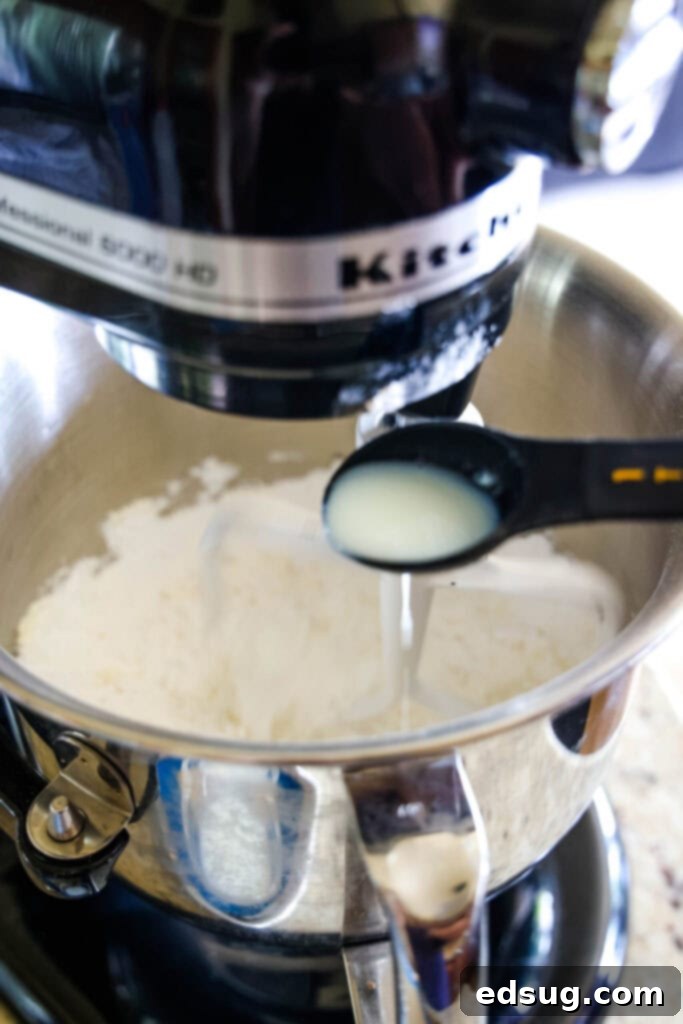 A teaspoon pouring milk into a stand mixer bowl with frosting