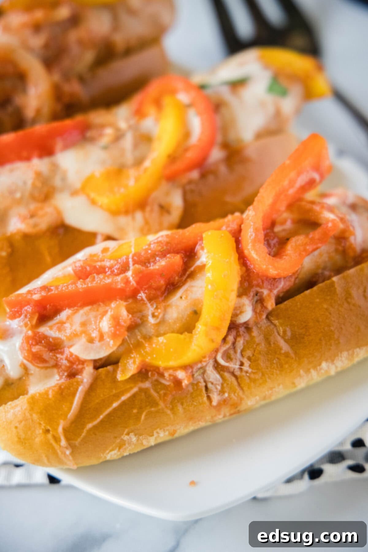 Two enticing sausage and pepper sandwiches served on a plate, showcasing melted cheese and tender ingredients.