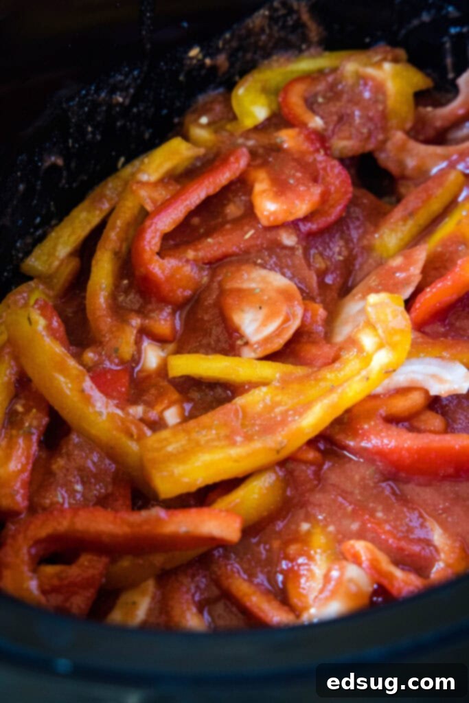 Sliced onions and peppers mixed with vibrant marinara sauce at the bottom of a crock pot, ready for sausage.