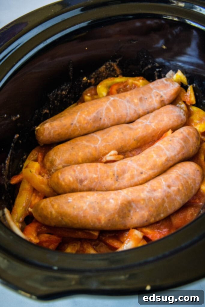 Four Italian sausage links placed neatly on top of the pepper, onion, and marinara mixture in a crock pot.