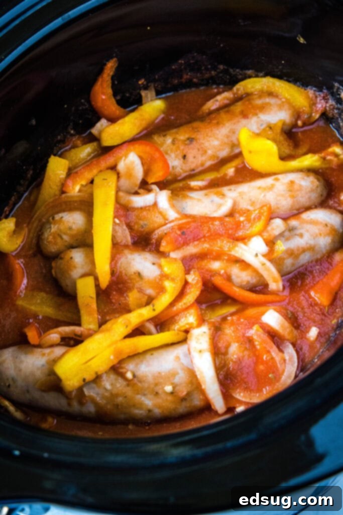 Fully cooked sausage, peppers, onions, and tomato sauce, simmering together in a crock pot, creating a hearty meal.