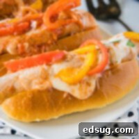 A plate with two sandwiches stuffed with sausage and peppers and melted cheese.