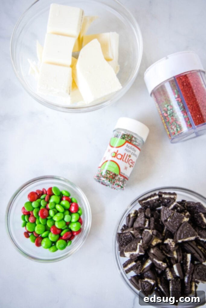 Holiday Candy Bark 3 Close-up shot of all the Christmas bark ingredients laid out: white chocolate almond bark, Oreo cookies, red and green M&M's, and festive sprinkles.