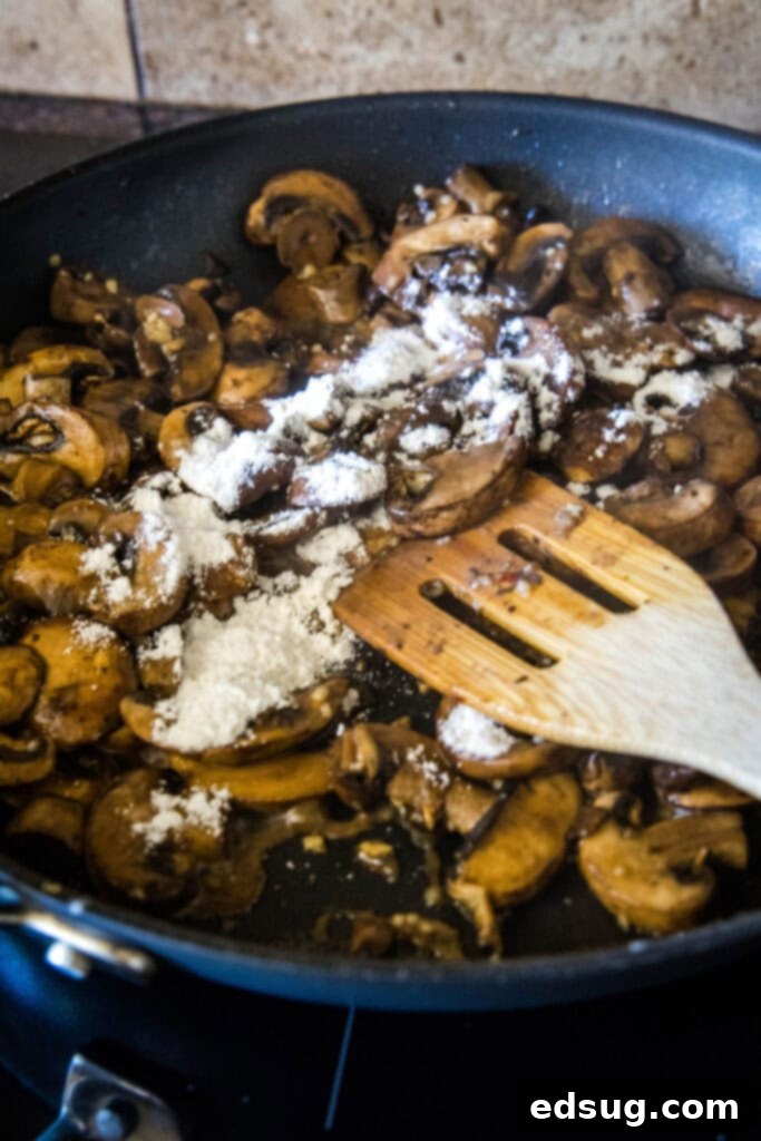 Easy and comforting chicken with mushroom sauce has juicy and tender meat smothered in a rich, herbaceous, and garlicky mushroom cream sauce. A wooden spatula stirring flour and mushrooms in a skillet