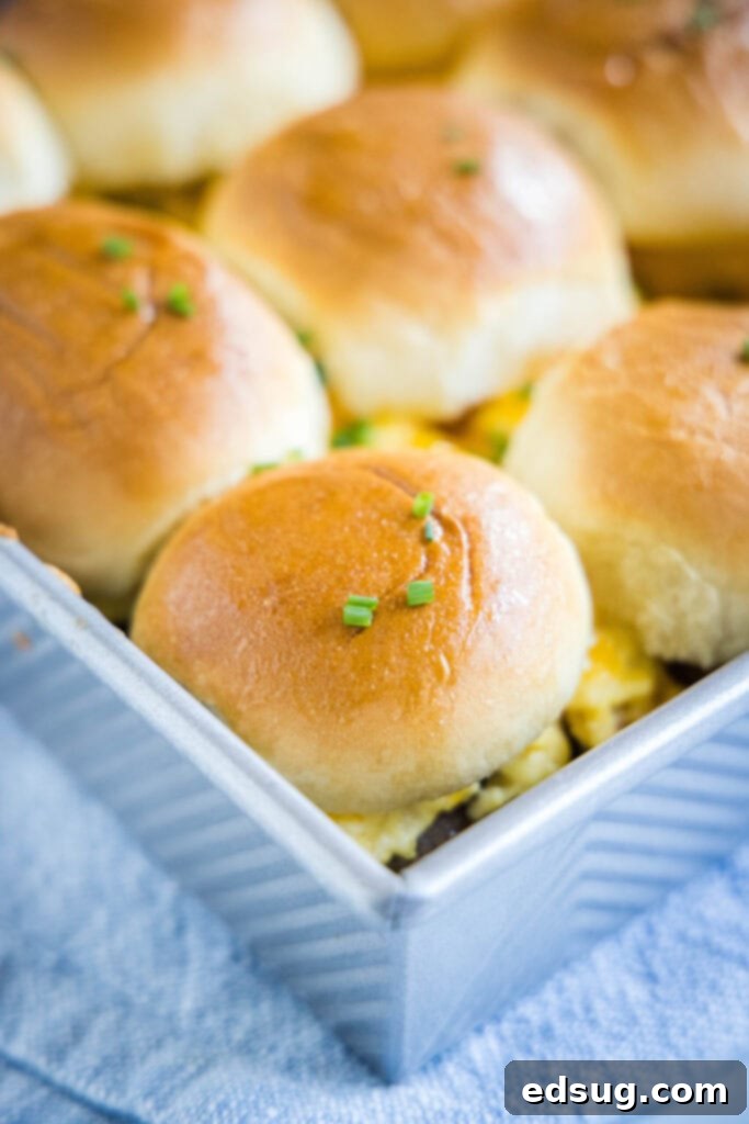 Close-up of baked breakfast sliders in a baking tray, garnished with fresh chives, ready to be served.