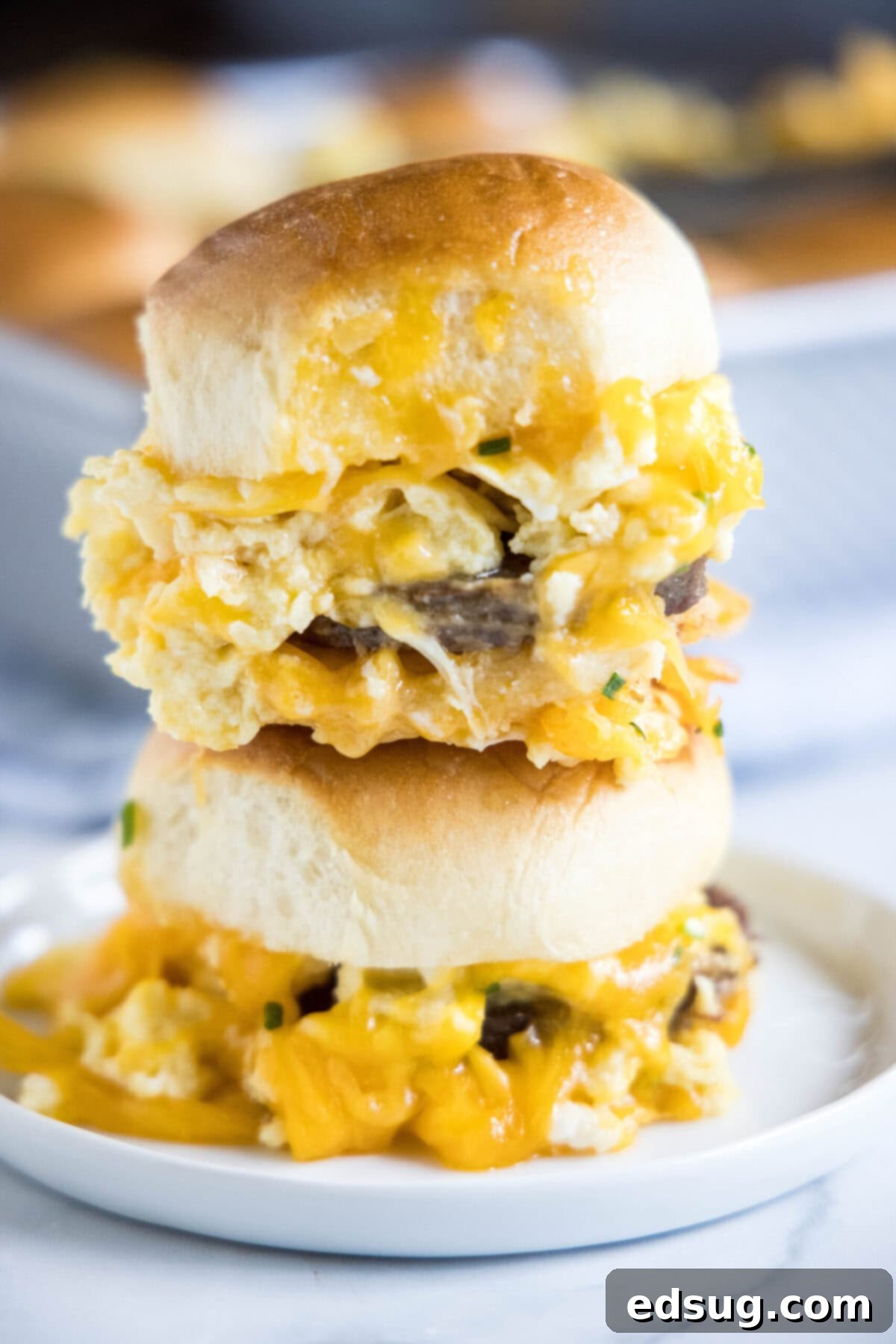 A plate featuring two perfectly stacked breakfast sliders, showing the layers of egg, sausage, and melted cheese between the buns.