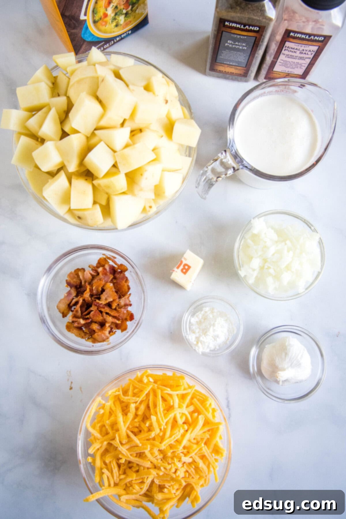 With a creamy broth, hearty chunks of potatoes, gooey cheese, and crispy bacon, this Instant Pot potato soup is the ultimate comfort meal. Overhead view of the ingredients needed for Instant Pot potato soup: a bowl of chopped potatoes, a bowl of shredded cheese, a bowl of crumbled bacon, a pyrex of cream, a bowl of onions, a bowl of garlic, a bowl of cornstarch, som butter, a carton of chicken stock, and salt and pepper grinders.