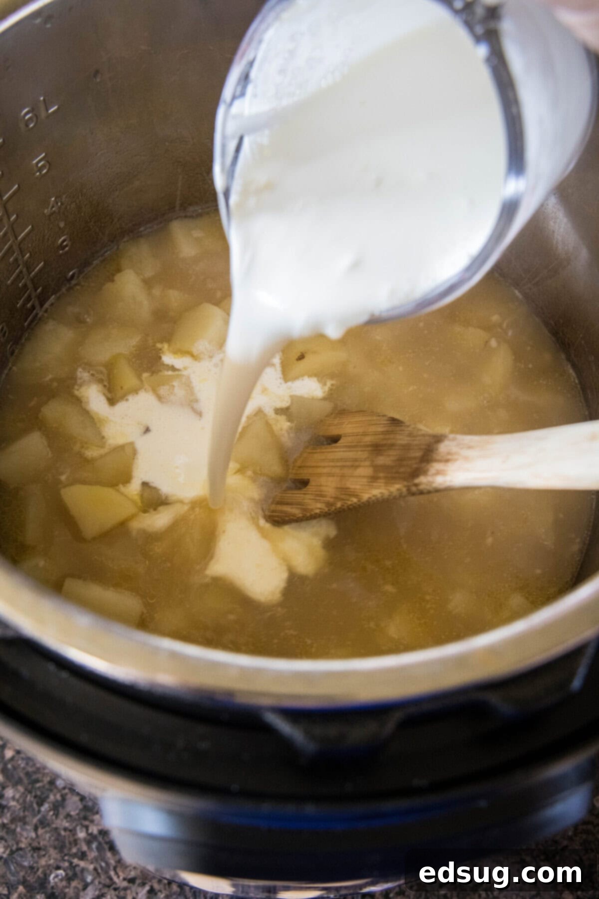 With a creamy broth, hearty chunks of potatoes, gooey cheese, and crispy bacon, this Instant Pot potato soup is the ultimate comfort meal. A pyrex pouring cream into a pot of potato soup with a wooden spoon.