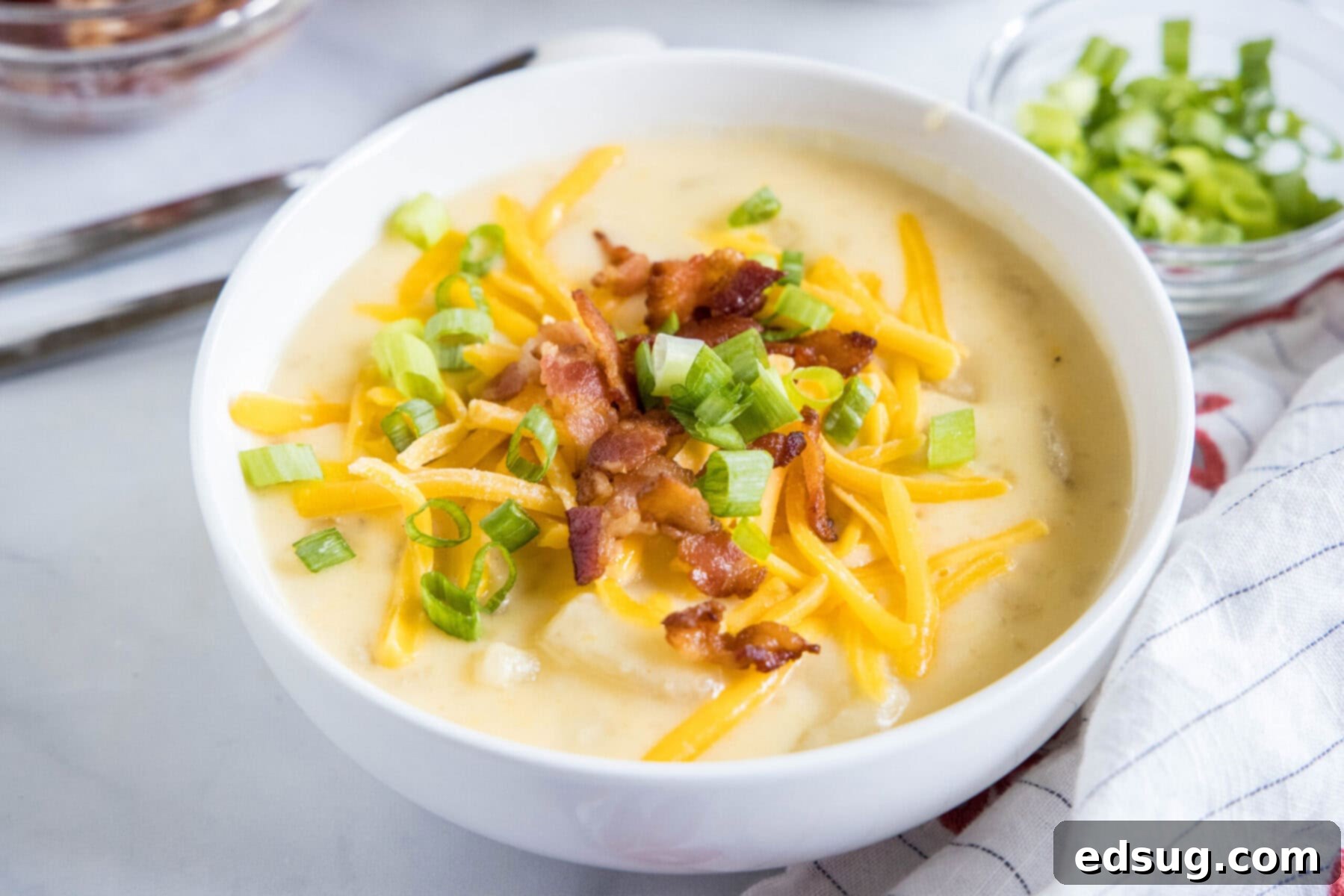 With a creamy broth, hearty chunks of potatoes, gooey cheese, and crispy bacon, this Instant Pot potato soup is the ultimate comfort meal. A bowl of potato soup topped with green onions, cheese, and bacon, next to a bowl of green onions.