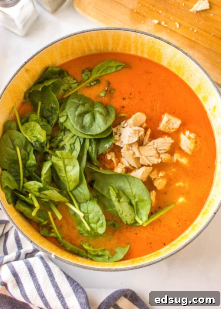 Fragrant Thai Red Curry Soup 4 A hand adding fresh spinach and cooked chicken back into a pot of simmering soup.