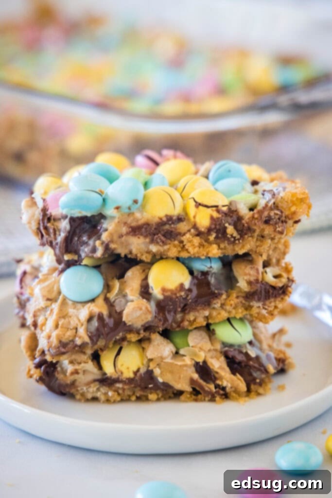 A stack of colorful Easter Magic Bars on a white plate, showcasing layers of graham crackers, peanut butter, chocolate, and festive M&M's.