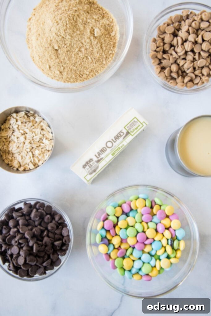 A collection of Easter Magic Bar ingredients including graham cracker crumbs, butter, oats, chocolate chips, peanut butter chips, sweetened condensed milk, and Easter M&M's.