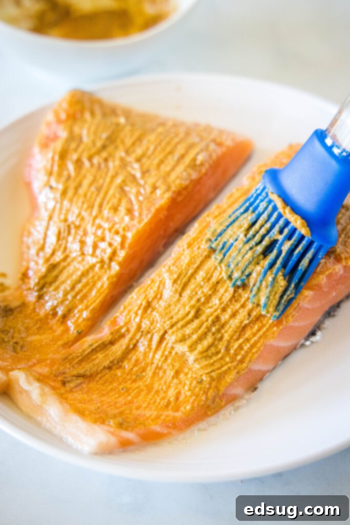 A brush rubbing a mustard spread on two raw salmon fillets.