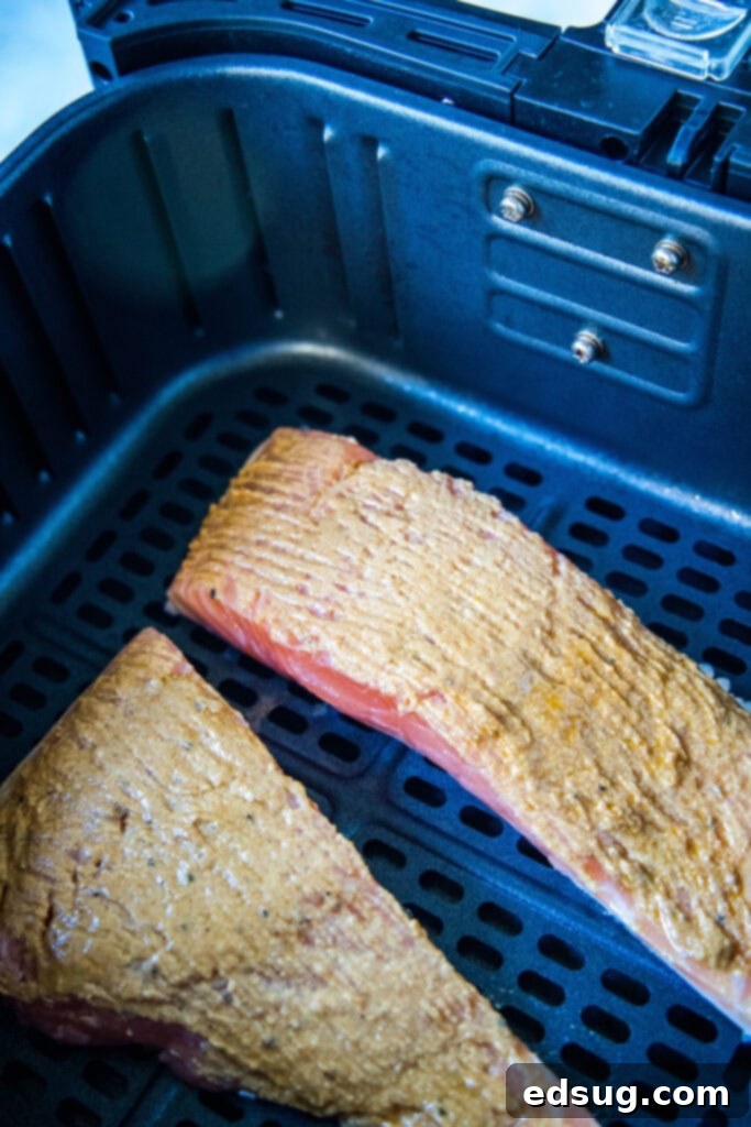 Two uncooked salmon fillets covered with a mustard rub in an air fryer basket.