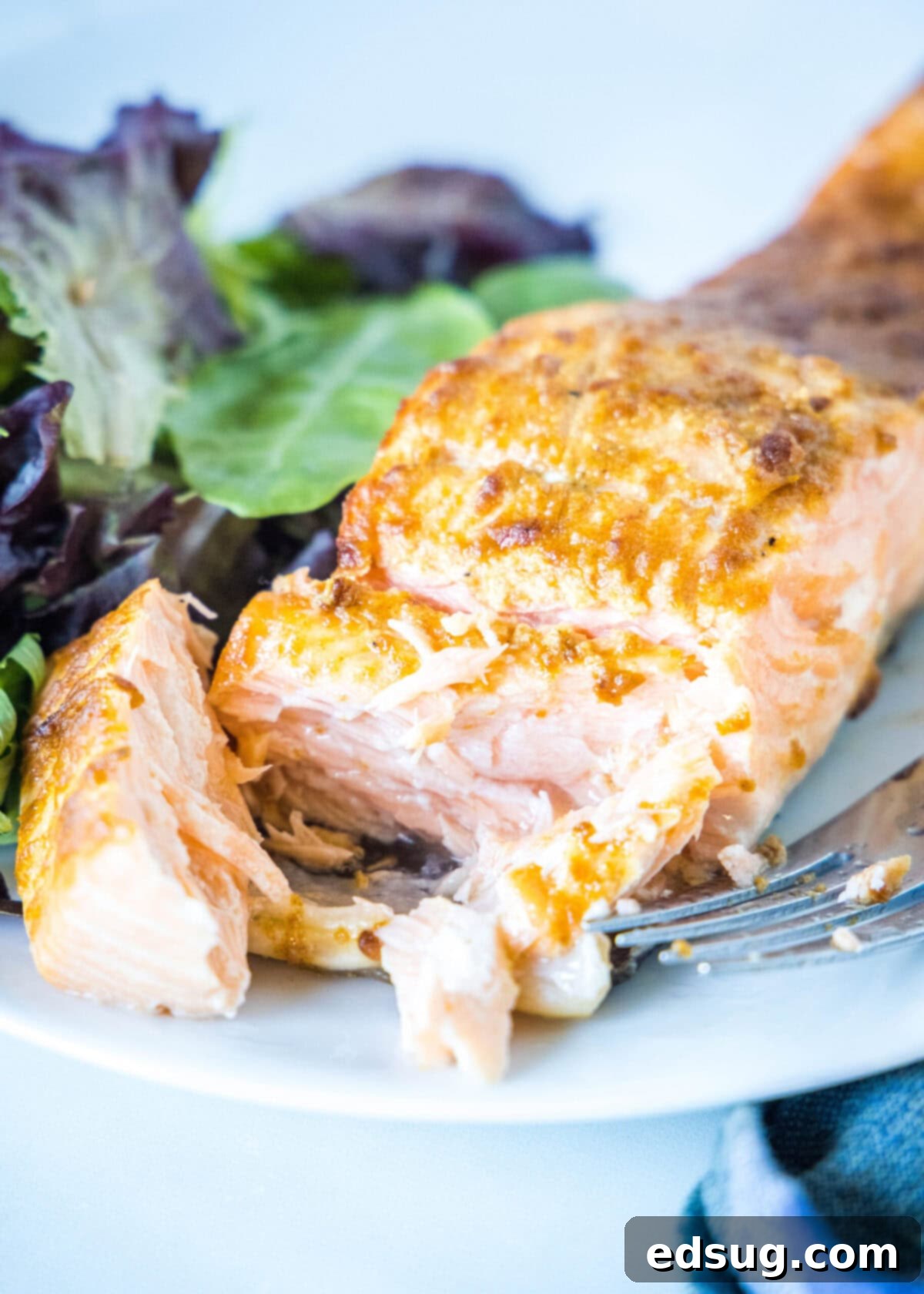 Close up of a fork cutting through a salmon fillet on a plate with a salad.