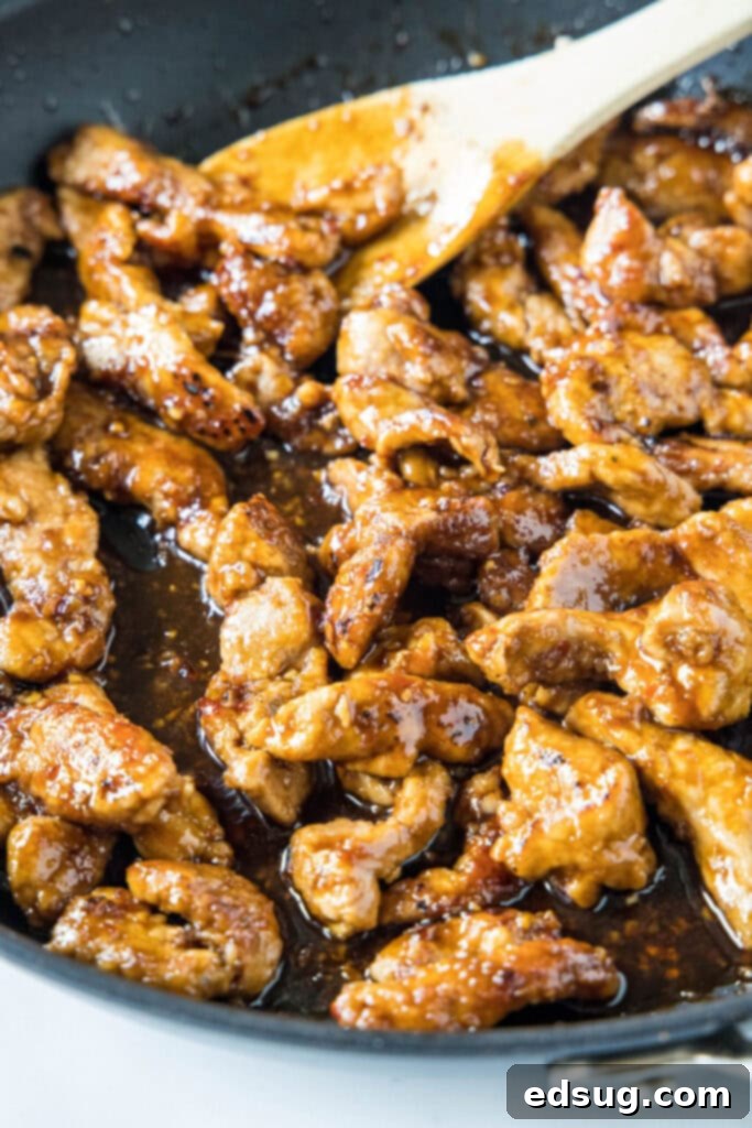 This Mongolian pork is tender, juicy, sweet, sour, a little bit spicy, and so much better than takeout, plus it only takes 20 minutes. Close up of pork cooking in a thick, brown sauce in a skillet, with a wooden spoon.