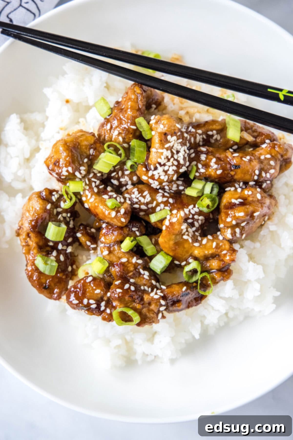 This Mongolian pork is tender, juicy, sweet, sour, a little bit spicy, and so much better than takeout, plus it only takes 20 minutes. Overhead view of a bowl of rice topped with Mongolian pork, green onions, and sesame seeds, with a pair of chopsticks.