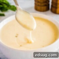 Close up of a spoonful of homemade cream of chicken soup hovering over a full bowl, garnished with a sprig of fresh parsley, with salt and pepper grinders in the soft-focus background, inviting viewers to taste the rich, velvety texture.