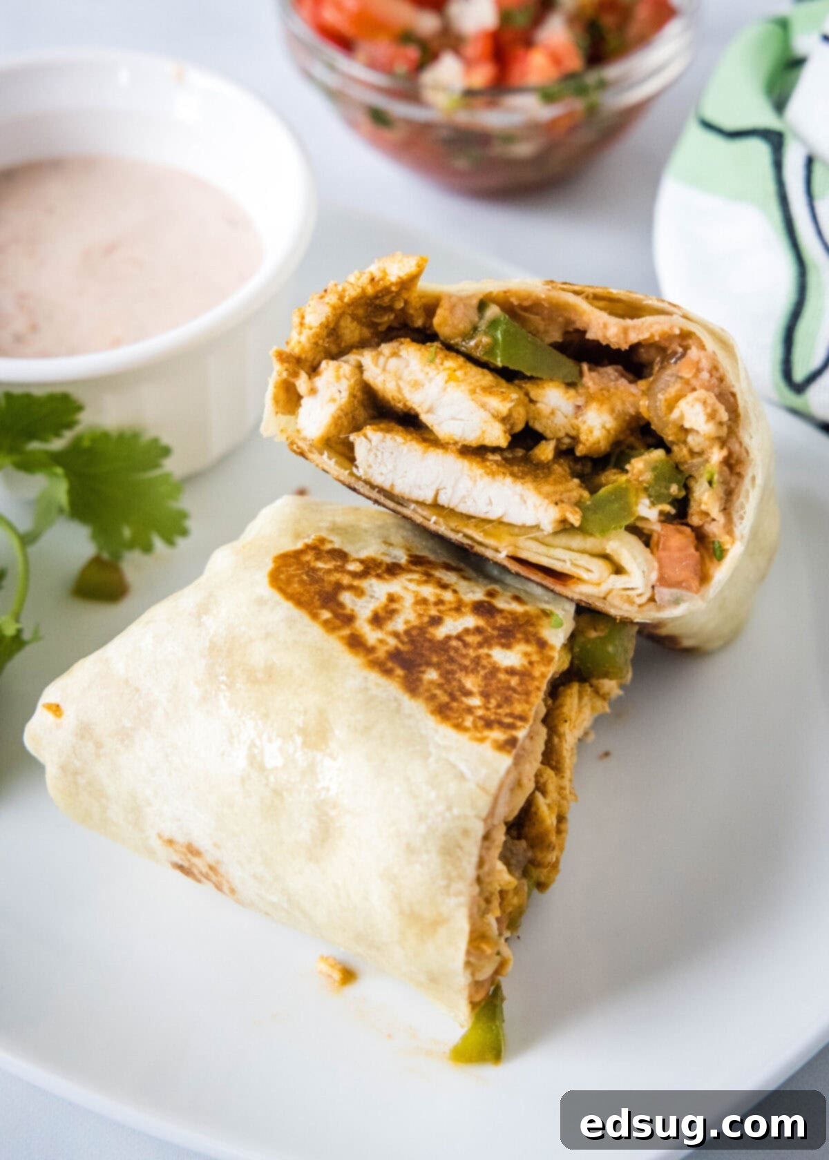 Easy chicken fajita wraps have juicy meat, tender veggies, spicy and smoky seasonings, rich beans, shredded cheese, and fresh salsa. One half of a chicken fajita wrap leaned against another half, next to a bowl of sauce and a bowl of salsa.