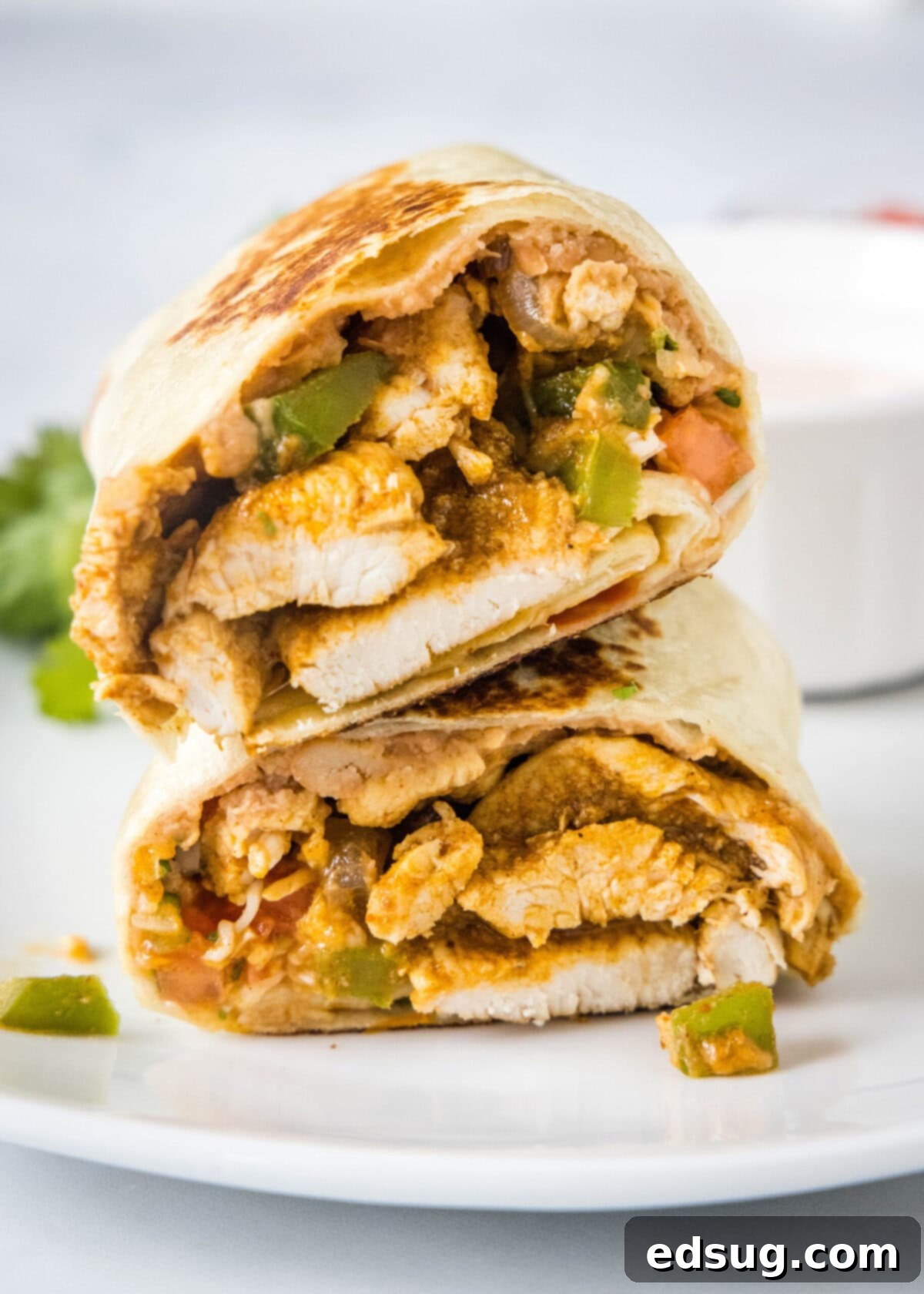 Easy chicken fajita wraps have juicy meat, tender veggies, spicy and smoky seasonings, rich beans, shredded cheese, and fresh salsa. Two halves of a chicken fajita wrap stacked on top of each other.