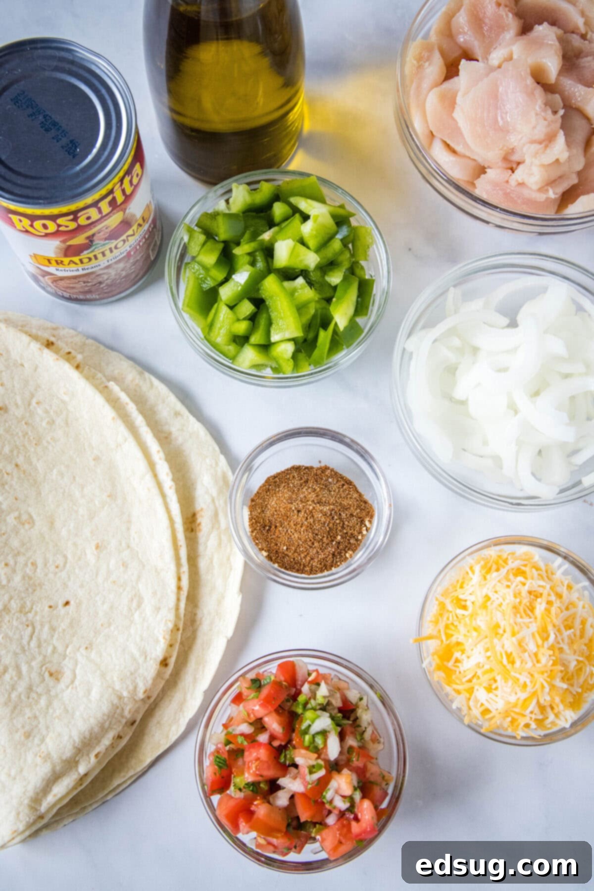 Easy chicken fajita wraps have juicy meat, tender veggies, spicy and smoky seasonings, rich beans, shredded cheese, and fresh salsa. Overhead view of the ingredients needed for chicken fajita wraps: a stack of tortillas, a can of refried beans, a bottle of olive oil, a bowl of chicken, a bowl of onions, a bowl of green peppers, a bowl of shredded cheese, a bowl of pico de gallo, and a bowl of spices.