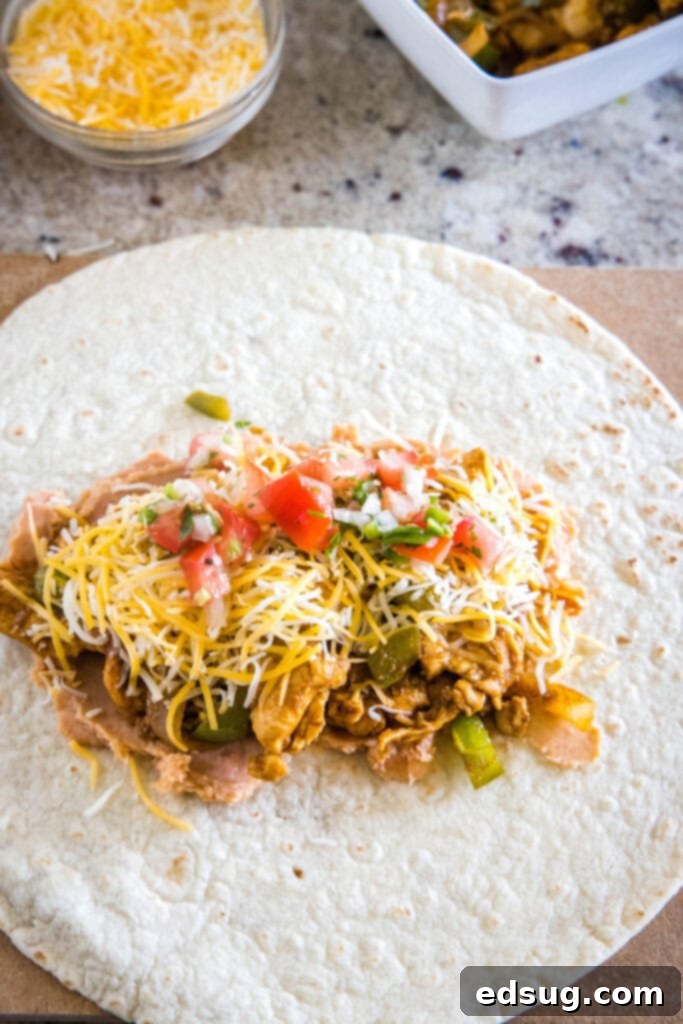 Easy chicken fajita wraps have juicy meat, tender veggies, spicy and smoky seasonings, rich beans, shredded cheese, and fresh salsa. A tortilla topped with beans, chicken and veggies, cheese, and pico de gallo.