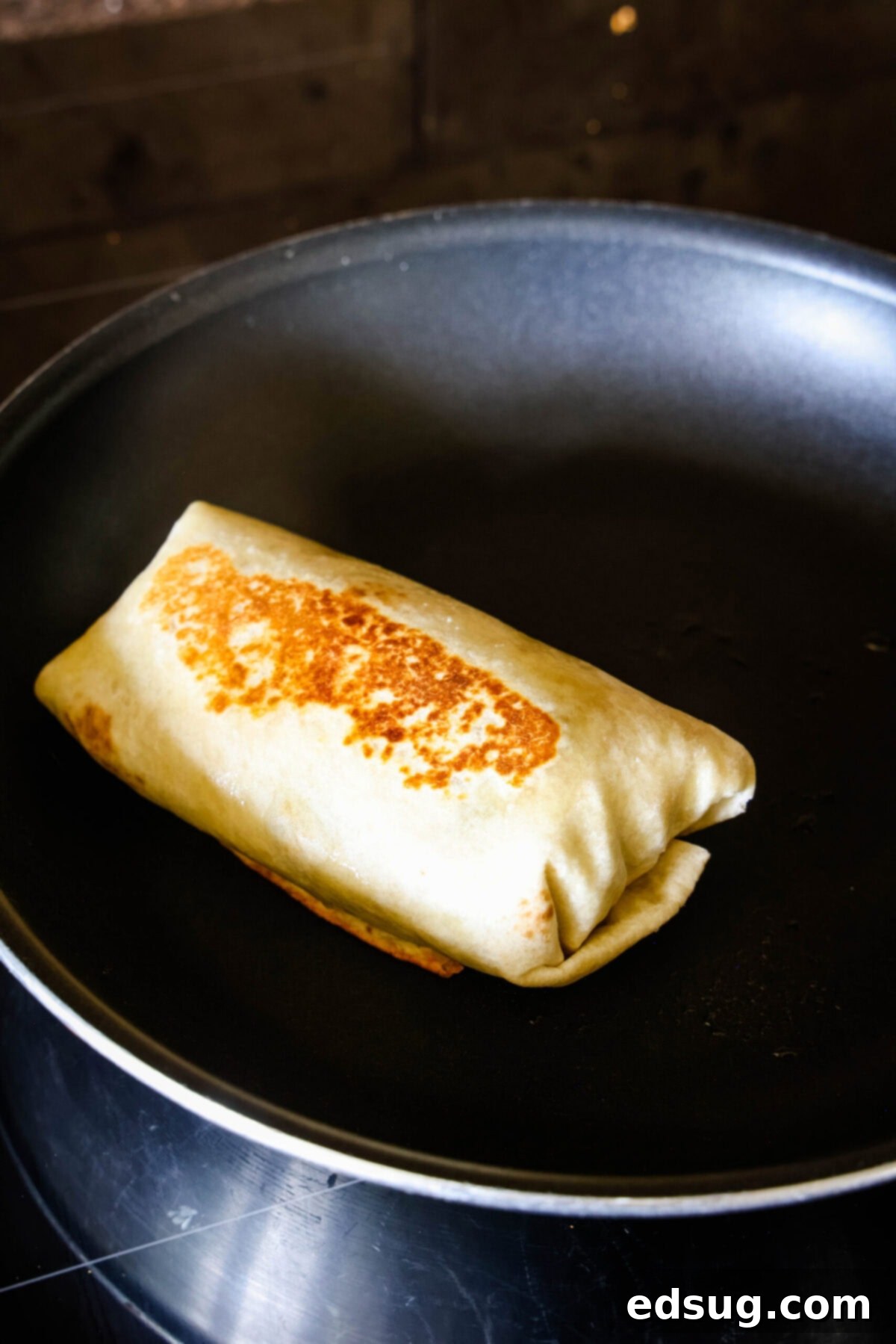 Easy chicken fajita wraps have juicy meat, tender veggies, spicy and smoky seasonings, rich beans, shredded cheese, and fresh salsa. A fajita wrap searing in a pan.