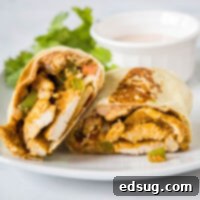 Cross section of a chicken fajita wrap cut in half on a plate, with lettuce and a bowl of sauce in the background.
