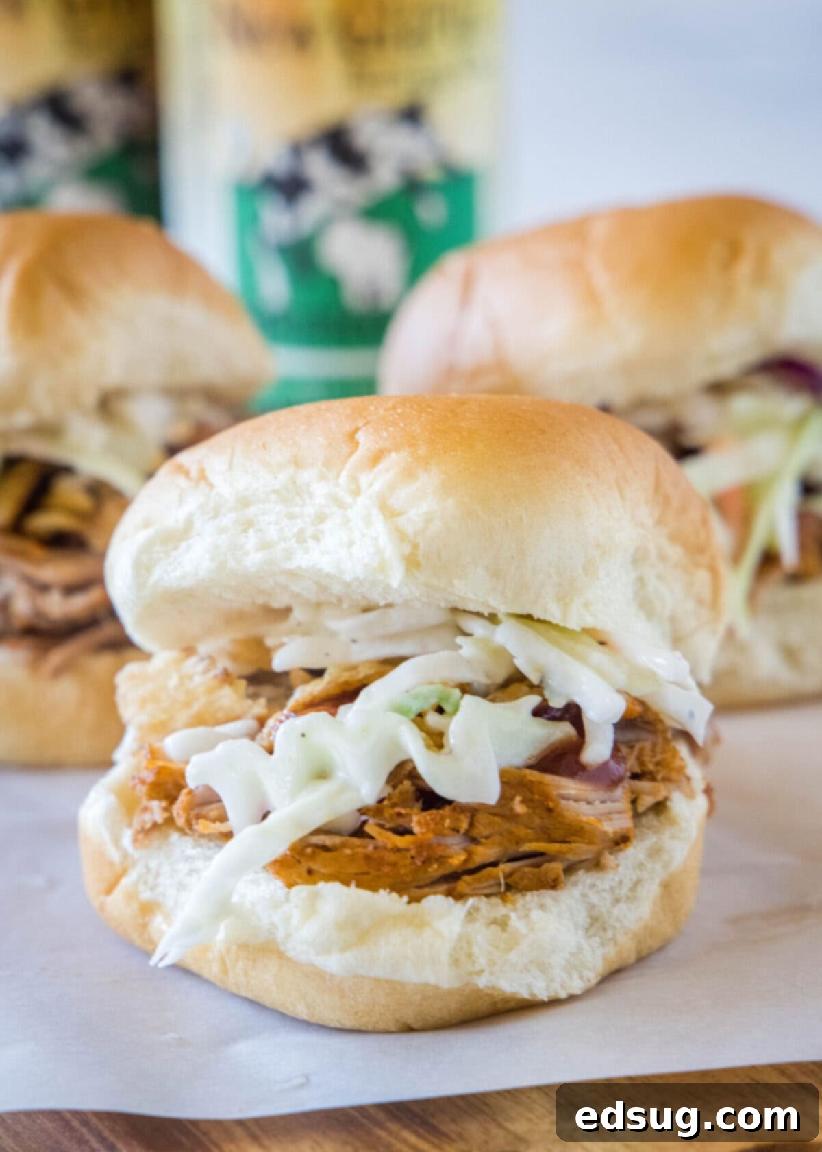 These easy pulled pork sliders boast tender and juicy meat, richly topped with smoky BBQ sauce, and a fresh, crunchy, tangy coleslaw. Close up of a pulled pork slider with creamy coleslaw, with two more perfectly assembled sliders blurred in the background, ready to be enjoyed.