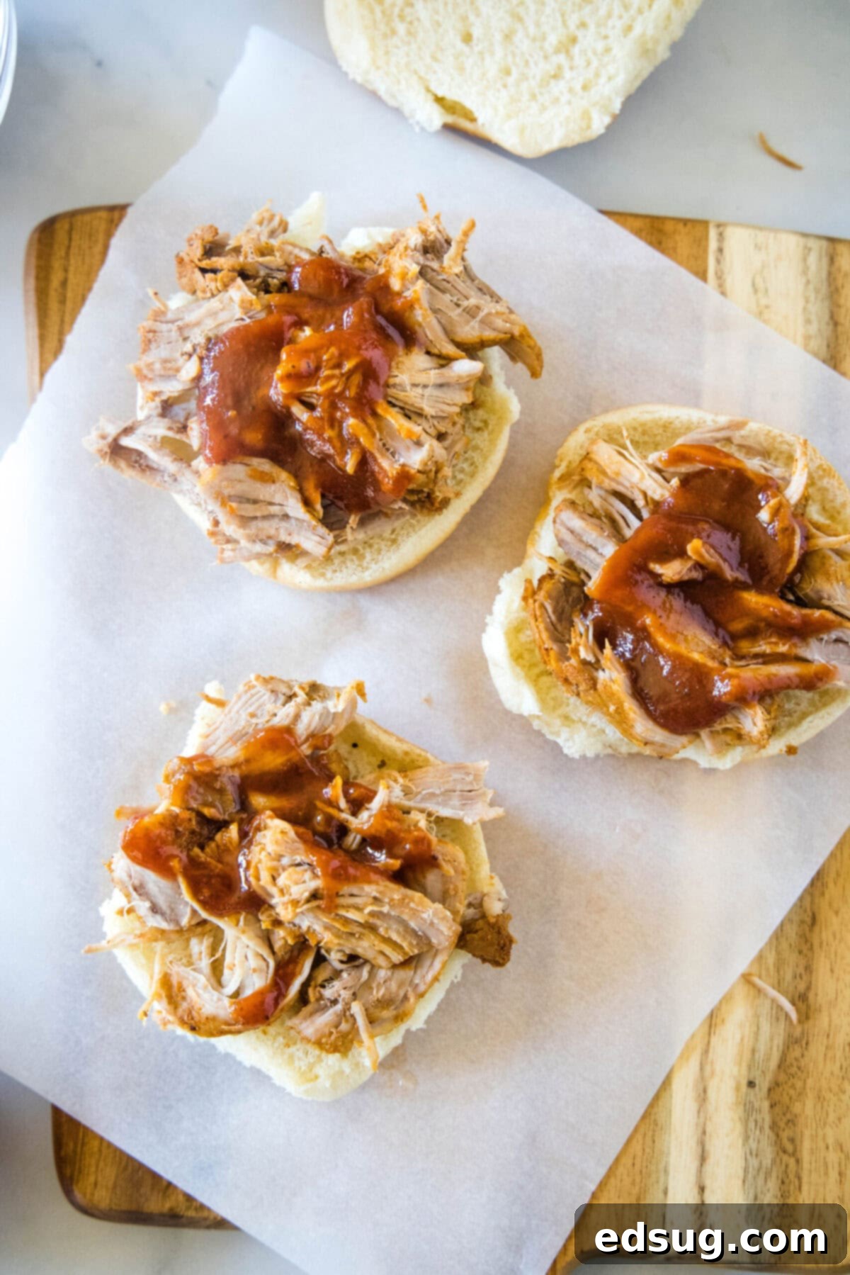 The foundation of easy pulled pork sliders: tender and juicy meat, topped with smoky BBQ sauce, on soft buns. An overhead view showing three bottom slider buns generously topped with perfectly shredded pulled pork and drizzled with smoky barbecue sauce, ready for the next layer of toppings.