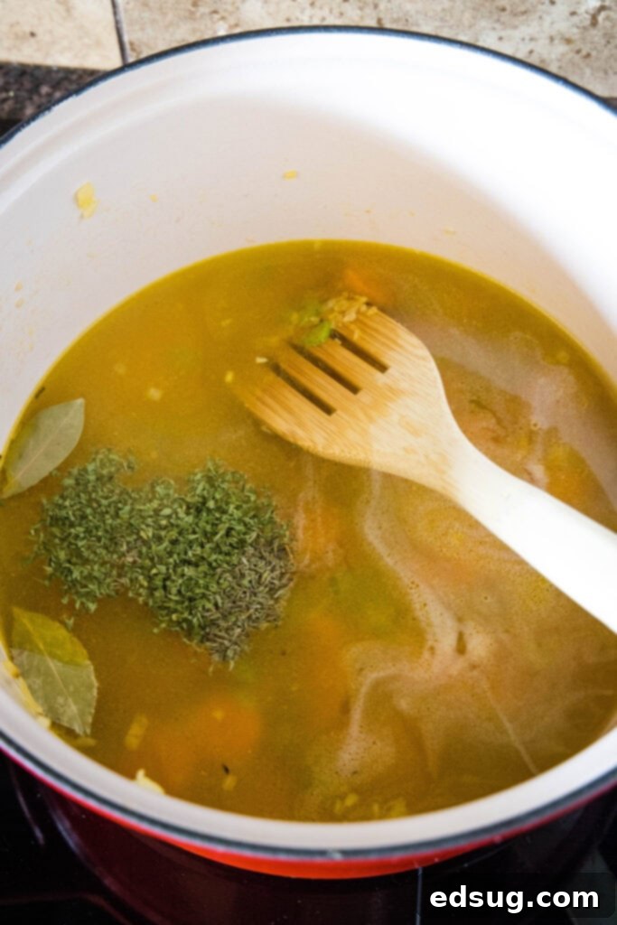 Building the Broth Base for Chicken Rice Soup. Chicken broth, dried parsley, thyme, and a bay leaf being added to the pot of sautéed vegetables, ready to simmer.